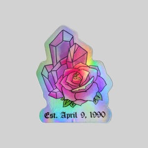May include: A holographic sticker featuring a pink rose and purple crystals. The sticker has the text "Est. April 9, 1990" at the bottom.