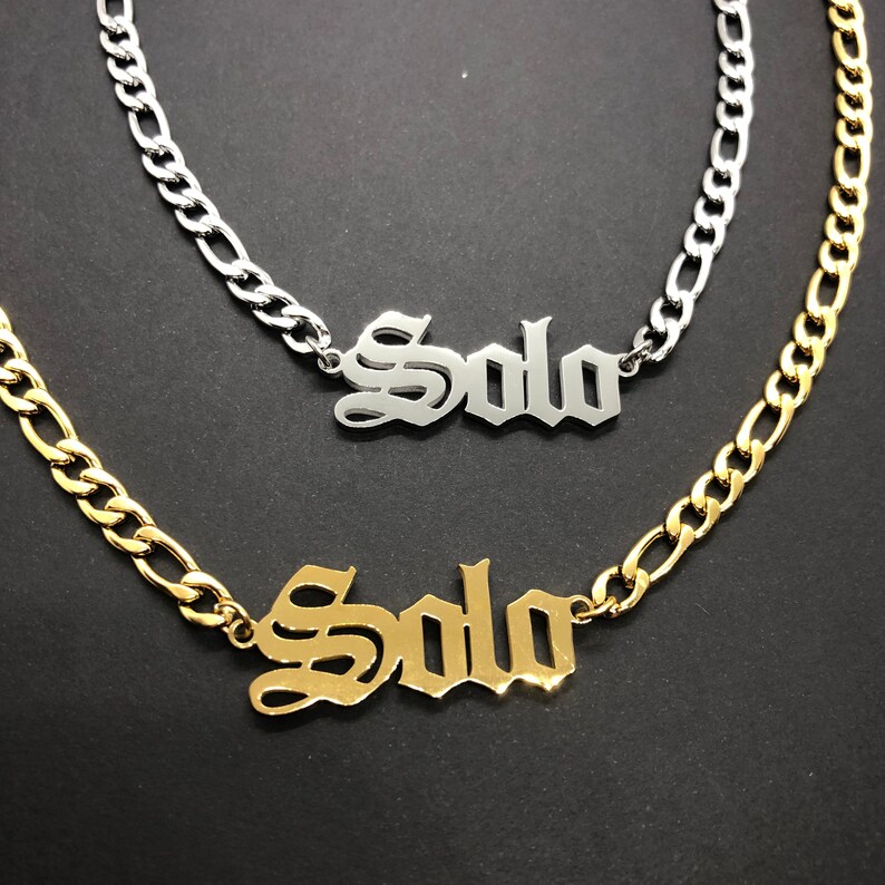 K&ouml;nnte beinhalten: Zwei goldene Ketten mit dem Namen "Solo" in alt-englischer Schrift. Die obere Kette ist silber und die untere Kette ist gold.