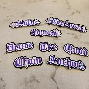 May include: Purple and white stickers with nautical themed words such as "Solo", "Captain", "Deuce", "Tre", "Quad", "Chain", "Anchor", and "Cap Anchor".