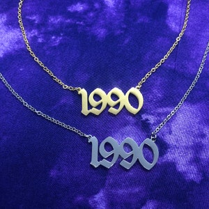May include: Two necklaces with the year 1990 in a gothic font. The top necklace is gold and the bottom necklace is silver.