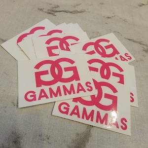 May include: A stack of white square stickers with a pink "FG" logo and the text "GAMMAS" printed on them.