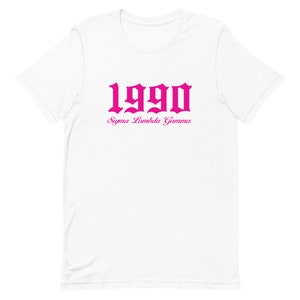 Op de afbeelding: Wit T-shirt met een roze 1990 in gotische letter en de tekst "Sigma Lambda Gamma" eronder.