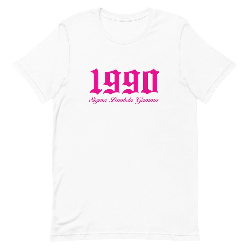 Op de afbeelding: Wit T-shirt met een roze 1990 in gotische letter en de tekst "Sigma Lambda Gamma" eronder.