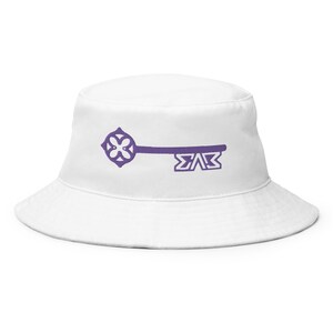 Può includere: Un cappello a secchiello bianco con una chiave viola e le lettere "ΣΑΣ" stampate sul davanti.