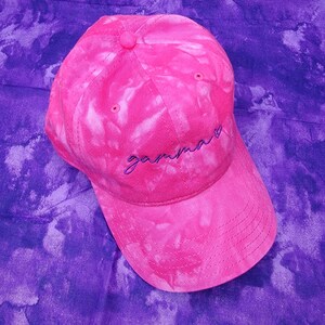 May include: Pink tie-dye baseball cap with purple embroidery that says "gamma".