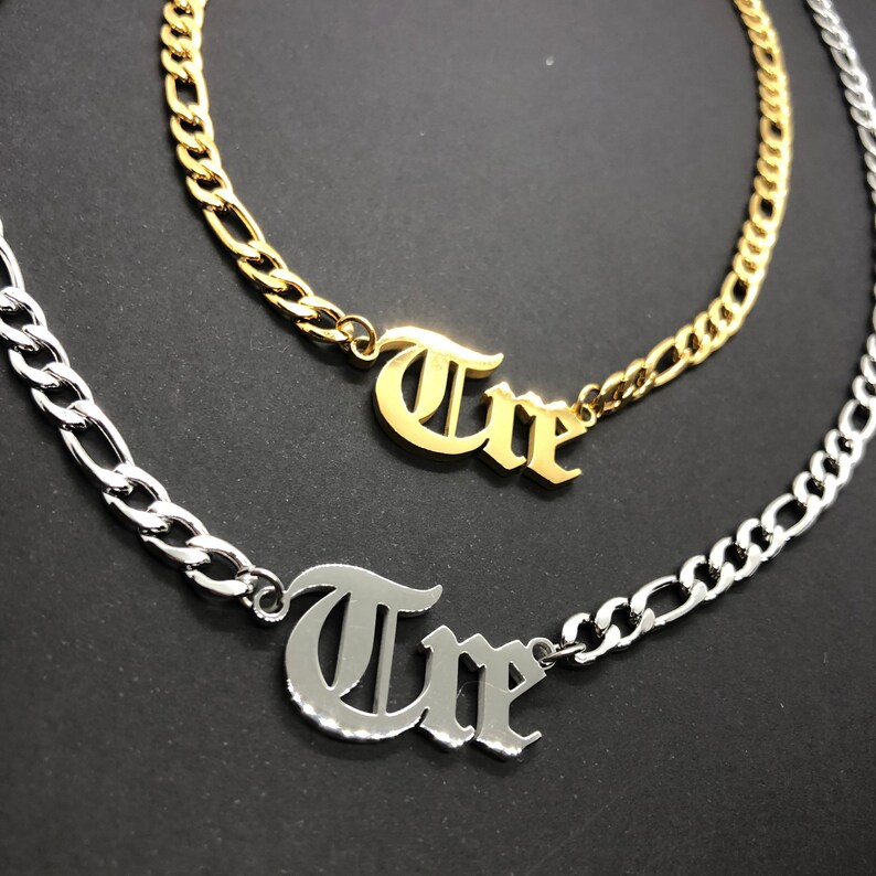 K&ouml;nnte beinhalten: Zwei goldene und silberne Ketten mit dem Wort "Tre" in altdeutscher Schrift.