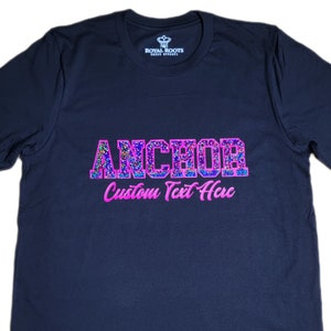 May include: A black t-shirt with a pink glitter design that says "ANCHOR" in large letters. Below the word "ANCHOR" is the text "Custom Text Here" in pink.
