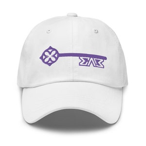 Puede incluir: Gorra de béisbol blanca con una llave bordada en morado y las letras "ΣΑΒ" en la parte delantera.