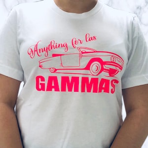 May include: White t-shirt with a pink graphic of a vintage car and the text "Anything for las GAMMAS".