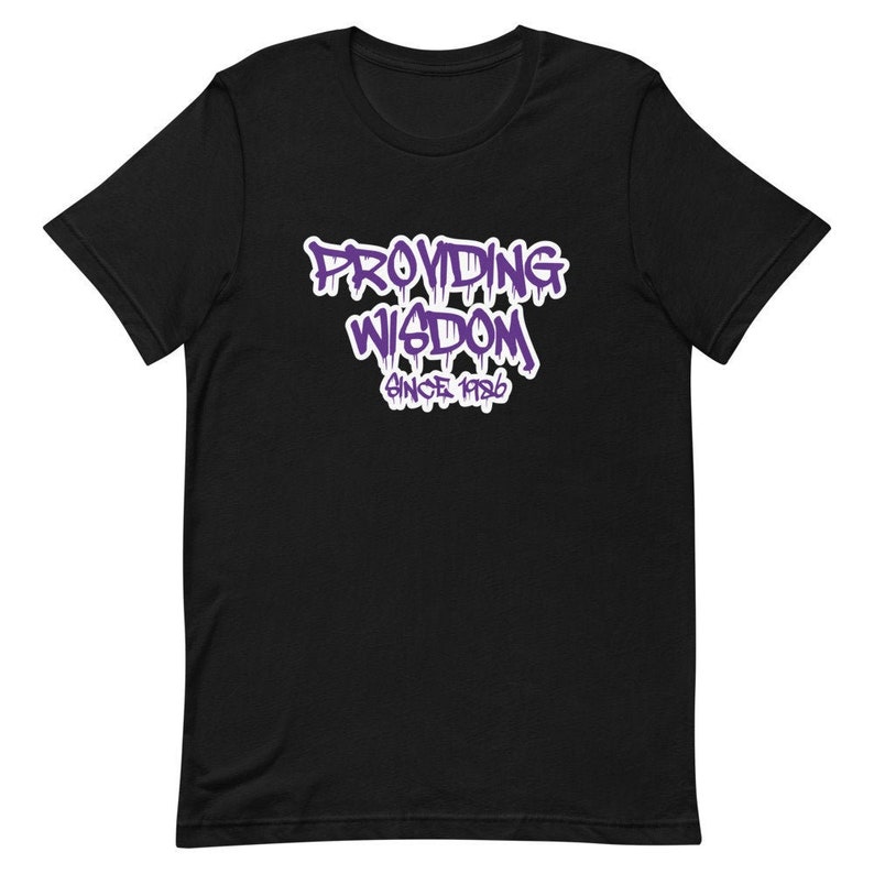 Op de afbeelding: Zwart T-shirt met een paarse grafische afbeelding met de tekst "Providing Wisdom Since 1986".
