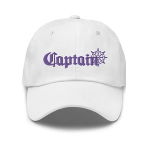 Puede incluir: Gorra de béisbol blanca con un logotipo bordado en morado que dice "Captain" con un timón de barco al lado.