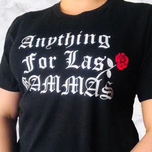 May include: Black t-shirt with the phrase "Anything For Las Mammas" in white gothic lettering. A red rose graphic is on the right side. The shirt is a crew neck style.