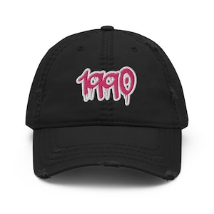 May include: A black distressed baseball cap with a pink and white embroidered "1990" graphic.