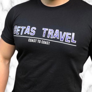 Könnte beinhalten: Schwarzes T-Shirt mit einer weißen und violetten Grafik, auf der "Betas Travel Coast to Coast" steht.