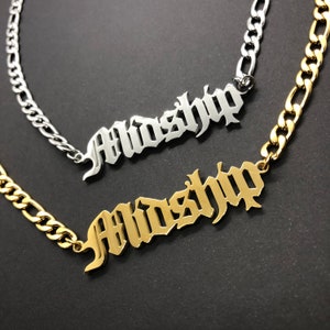 K&ouml;nnte beinhalten: Zwei goldene Ketten mit dem Wort "Midship" in gotischer Schrift. Die obere Kette ist silber und die untere Kette ist gold.