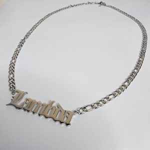 May include: Silver chain necklace with a large, silver pendant that says "Lambda" in a gothic font.