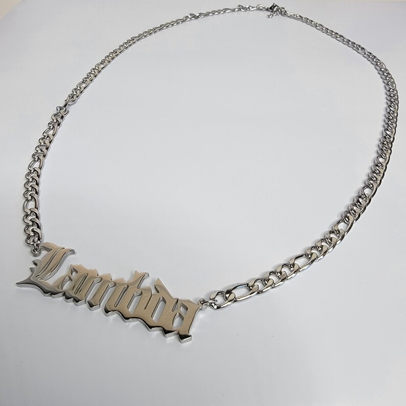 May include: Silver chain necklace with a large, silver pendant that says "Lambda" in a gothic font.
