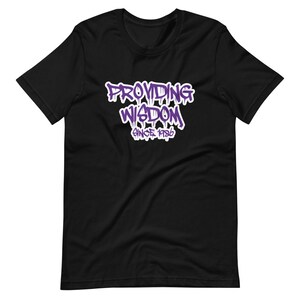 Op de afbeelding: Zwart T-shirt met een paarse grafische afbeelding met de tekst "Providing Wisdom Since 1986".