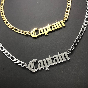 Könnte beinhalten: Zwei Halsketten, eine goldene und eine silberne, mit dem Wort "Captain" in gotischer Schrift.