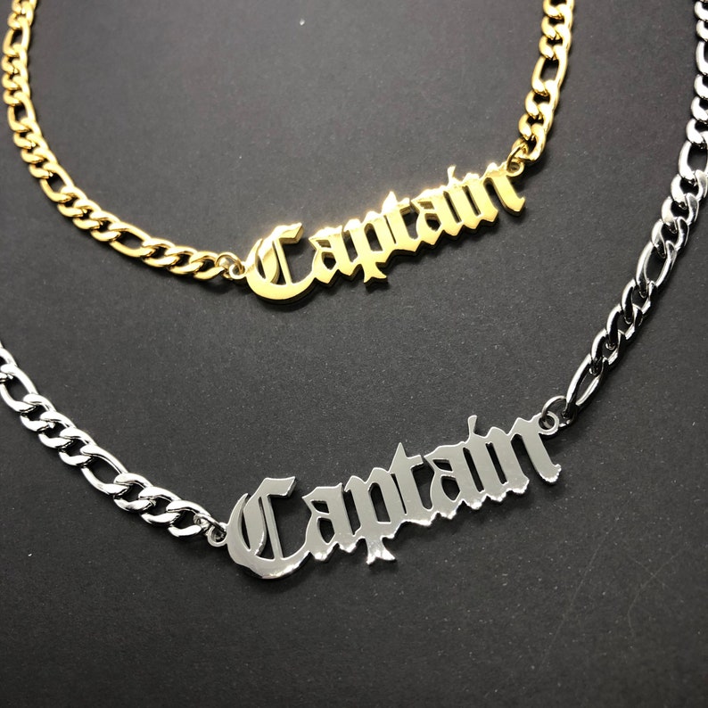 K&ouml;nnte beinhalten: Zwei Halsketten, eine goldene und eine silberne, mit dem Wort "Captain" in gotischer Schrift.