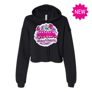 Puede incluir: Sudadera con capucha negra recortada con un diseño gráfico rosa y blanco que dice "Gamma, Woman of Distinction" con rosas rosas y detalles de purpurina.