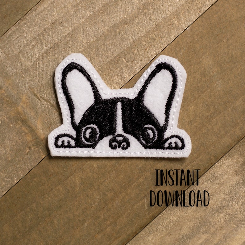 May include: Black and white embroidered design of a French bulldog peeking out from behind a white surface. The design is stitched with white thread on a white felt background.