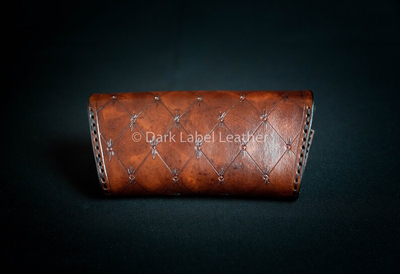 May include: A brown leather wallet with a diamond-shaped pattern and a stitched border. The wallet has the text "Dark Label Leather" embossed on the front.