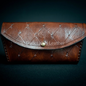 May include: A brown leather glasses case with a quilted design and a gold button closure. The case has a stitched border and the text "Dark Label Leather" is embossed on the front.