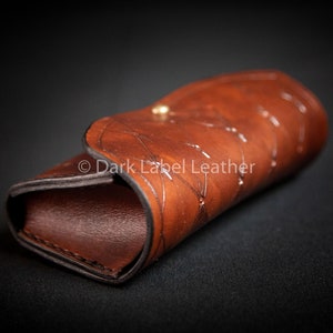 May include: A brown leather case with a decorative pattern and a gold button closure.  &copy; Dark Label Leather