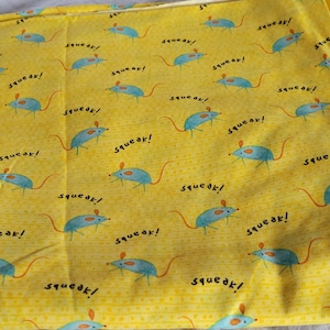 Pode incluir: Tecido amarelo com um padrão repetido de ratos azuis e a palavra "squeak!". Os ratos têm corpos azuis, orelhas cor-de-rosa e caudas longas. O tecido está dobrado.