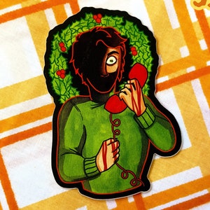 May include: A green and red sticker of a person with a black mask holding a red phone with a bloody hand. The person is wearing a green sweater and a holly wreath is behind their head. The sticker is 3.5 inches in diameter.