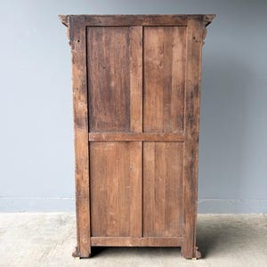 Puede incluir: Un panel trasero de armario alto y rectangular de madera con un acabado de veta de madera marr&oacute;n natural. La estructura se compone de tablones de madera verticales y horizontales enmarcados por un borde robusto, con tallas decorativas en las esquinas.