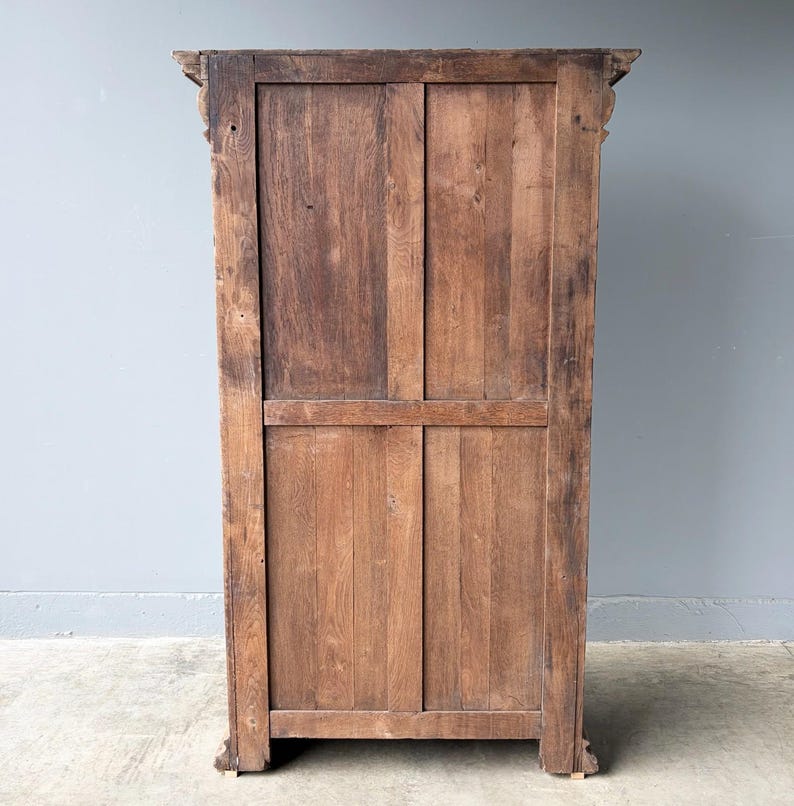 Puede incluir: Un panel trasero de armario alto y rectangular de madera con un acabado de veta de madera marr&oacute;n natural. La estructura se compone de tablones de madera verticales y horizontales enmarcados por un borde robusto, con tallas decorativas en las esquinas.