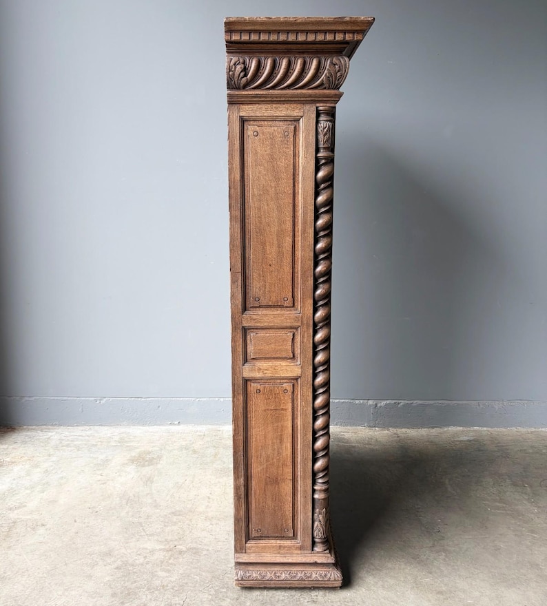 Puede incluir: Un panel lateral de armario de madera alto y estrecho con un acabado marr&oacute;n medio. La estructura incluye una cornisa superior tallada, un detalle de columna vertical retorcida y paneles rectangulares empotrados con pasadores visibles.