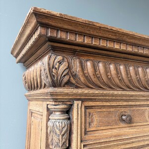 Puede incluir: Un mueble de madera de color marr&oacute;n claro con intrincados detalles tallados, incluyendo un friso decorativo con motivos de hojas y patrones estriados en el borde superior. La estructura incluye una columna vertical con follaje tallado y un caj&oacute;n.