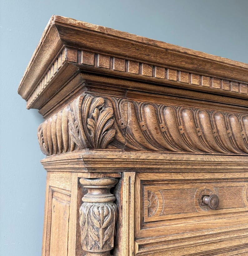 Puede incluir: Un mueble de madera de color marr&oacute;n claro con intrincados detalles tallados, incluyendo un friso decorativo con motivos de hojas y patrones estriados en el borde superior. La estructura incluye una columna vertical con follaje tallado y un caj&oacute;n.