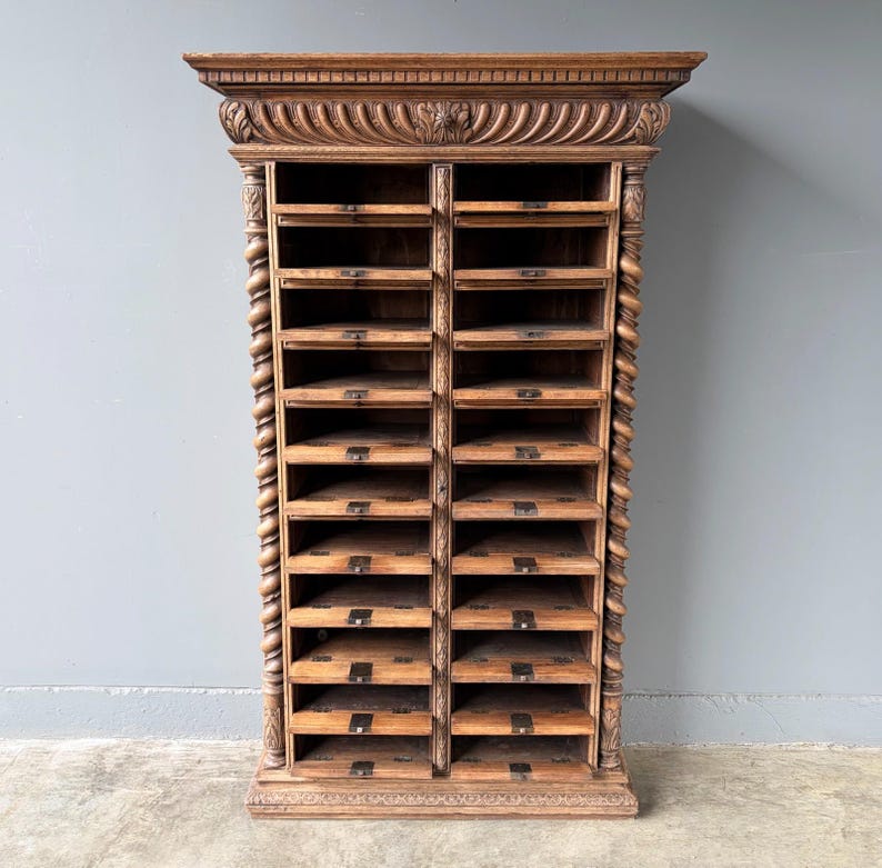 Puede incluir: Un armario alto de madera marr&oacute;n con dos columnas verticales de compartimentos de almacenamiento abiertos. La pieza est&aacute; decorada con detalles tallados acanalados en la cornisa superior y columnas de estilo soga trenzada a los lados.