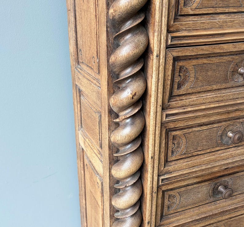 Puede incluir: Una c&oacute;moda alta de madera que presenta una prominente columna vertical con forma de espiral en el lateral. La pieza est&aacute; hecha de madera de color marr&oacute;n claro con vetas visibles e incluye varios cajones con peque&ntilde;os pomos redondos.