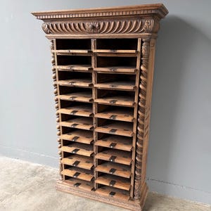 Puede incluir: Un armario alto de madera marr&oacute;n con dos columnas verticales de m&uacute;ltiples estantes de almacenamiento abiertos. La unidad est&aacute; decorada con molduras estriadas talladas en la parte superior y columnas de estilo soga retorcida en ambos lados, con peque&ntilde;os portaetiquetas.