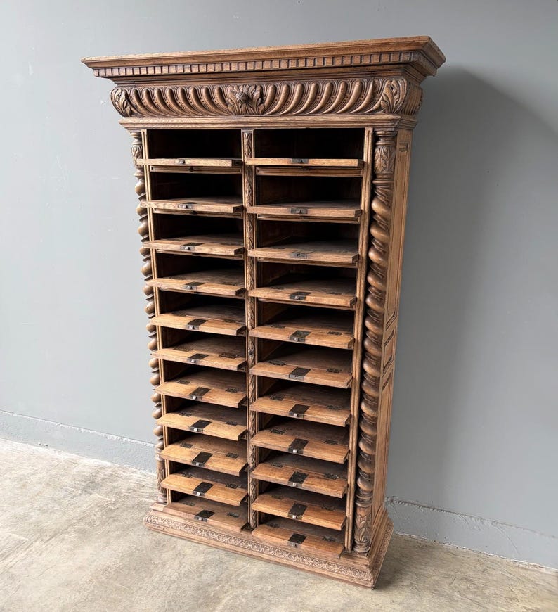 Puede incluir: Un armario alto de madera marr&oacute;n con dos columnas verticales de m&uacute;ltiples estantes de almacenamiento abiertos. La unidad est&aacute; decorada con molduras estriadas talladas en la parte superior y columnas de estilo soga retorcida en ambos lados, con peque&ntilde;os portaetiquetas.