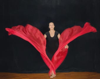 May include: A person in a black dress holds and moves a flowing, vibrant red fabric against a black backdrop. The fabric is labeled "Passion Red - Straight cut Medium". The fabric is draped and flowing, creating a dynamic visual.