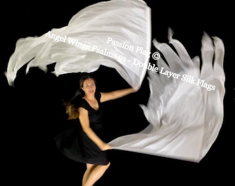 May include: A woman in a black dress dances with two large, flowing white silk flags against a black background. The flags are labeled "Passion Flags" and "Double Layer Silk Flags". The text "Angel Wings Psalms 91" is also visible.