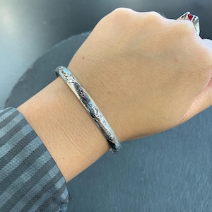 May include: A silver bangle bracelet with an intricate floral design.