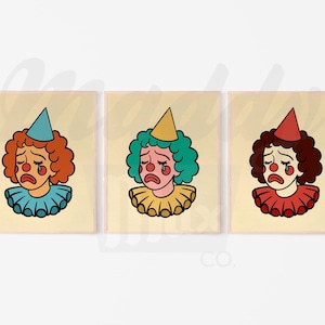 Puede incluir: Conjunto de tres impresiones enmarcadas con payasos de dibujos animados con expresiones tristes. Cada payaso tiene un color de pelo, un gorro de fiesta y un cuello con volantes diferentes. Fondo crema.