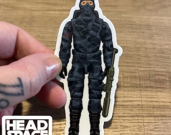 Könnte beinhalten: Eine blaue und schwarze Tarnfigur mit schwarzer Maske und grünem Gewehr. Die Figur hat ein rotes Cobra-Symbol auf der Brust.
