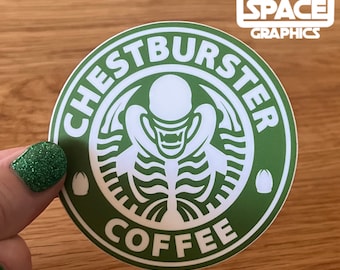 May include: A green and white sticker with the text "CHESTBURSTER COFFEE" in a circular design. The design features a skeletal alien figure. The sticker also includes the text "HEAD SPACE GRAPHICS" in a white square.