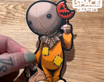 May include: A cartoon character dressed in orange with a stitched face and a burlap sack. The character is holding a bitten candy apple and a burlap sack. The character is a Halloween themed sticker.