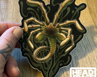 May include: A black and green alien creature sticker with a long tail and multiple legs. The creature is surrounded by a black background with green and white swirls.