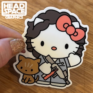 May include: A white Hello Kitty character with a pink bow, brown hair, and a gray jumpsuit, holding a gray and red gun. A brown cat is standing next to her.