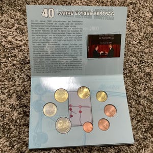 May include: A commemorative coin set celebrating 40 years of the Elysee Treaty. The set includes various Euro coins displayed on a light blue card with German text and a small photo. The coins are gold and copper-colored.